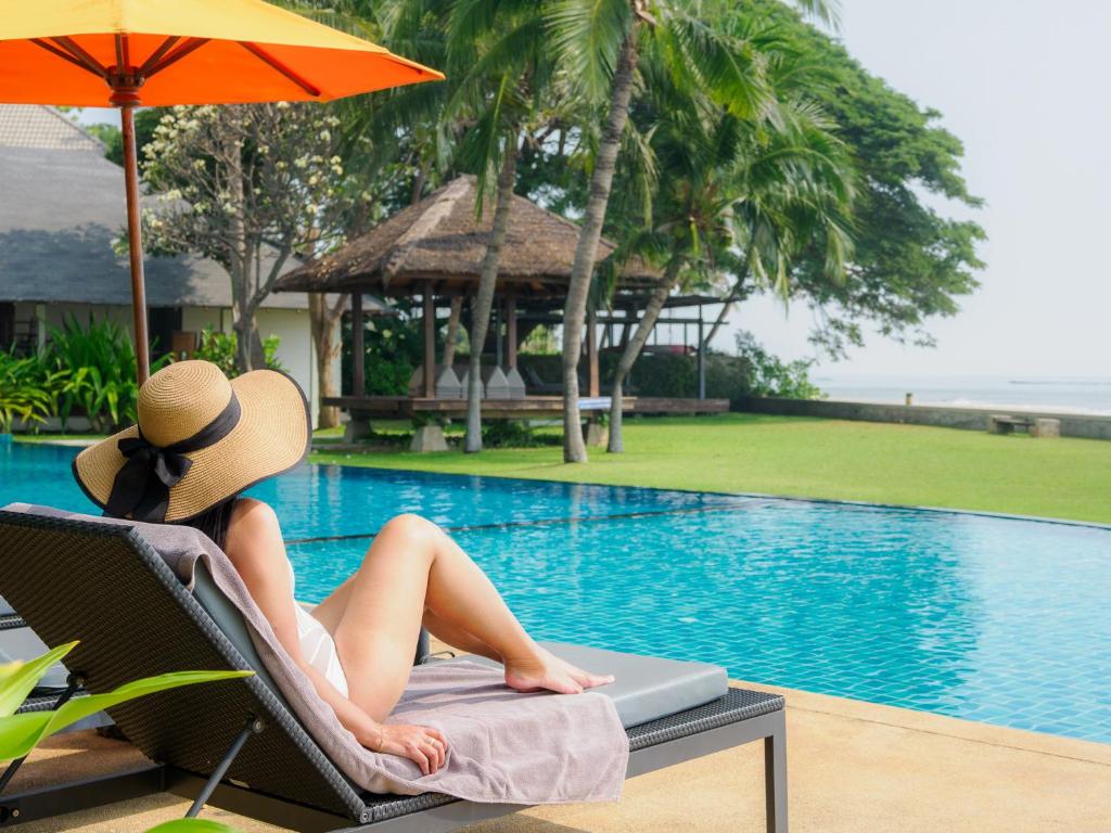 a woman in a hat sitting in a chair next to a swimming pool at Fisherman's Resort Haad Chao Samran in Haad Chao Samran