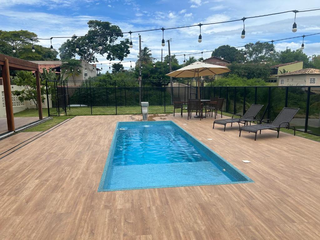 a swimming pool with chairs and a table and an umbrella at Casa de alto padrão com piscina,quadra e jacuzzi em condomínio in Guarapari