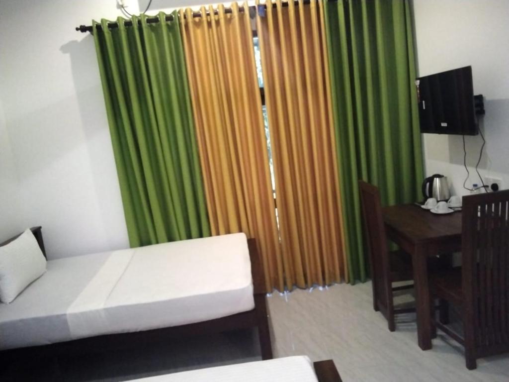 a living room with a couch and a table and green curtains at Aluthwewa Gate in Angunakolapelessa