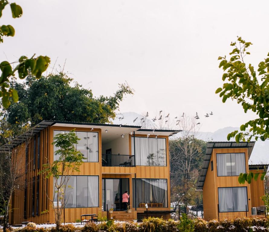 a house in the woods with a person standing on the balcony at Qudrat - Boutique Hostel & Cafe in Bīr