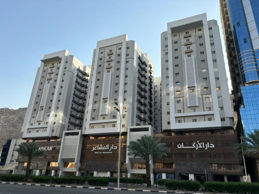 two tall white buildings with palm trees in front of a street at شقة في دار المشاعر in Mecca