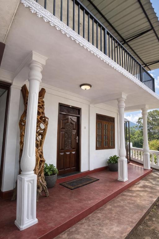a front porch with white columns and a wooden door at Ora Living in Maskeliya