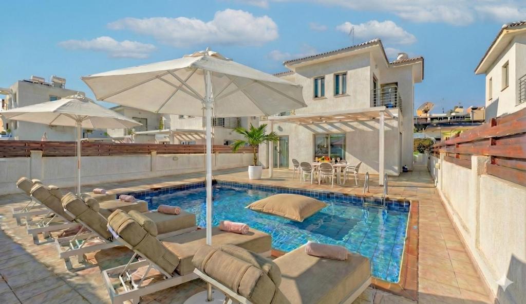 a swimming pool with lounge chairs and an umbrella at Fig Tree Beach Villa Four in Protaras