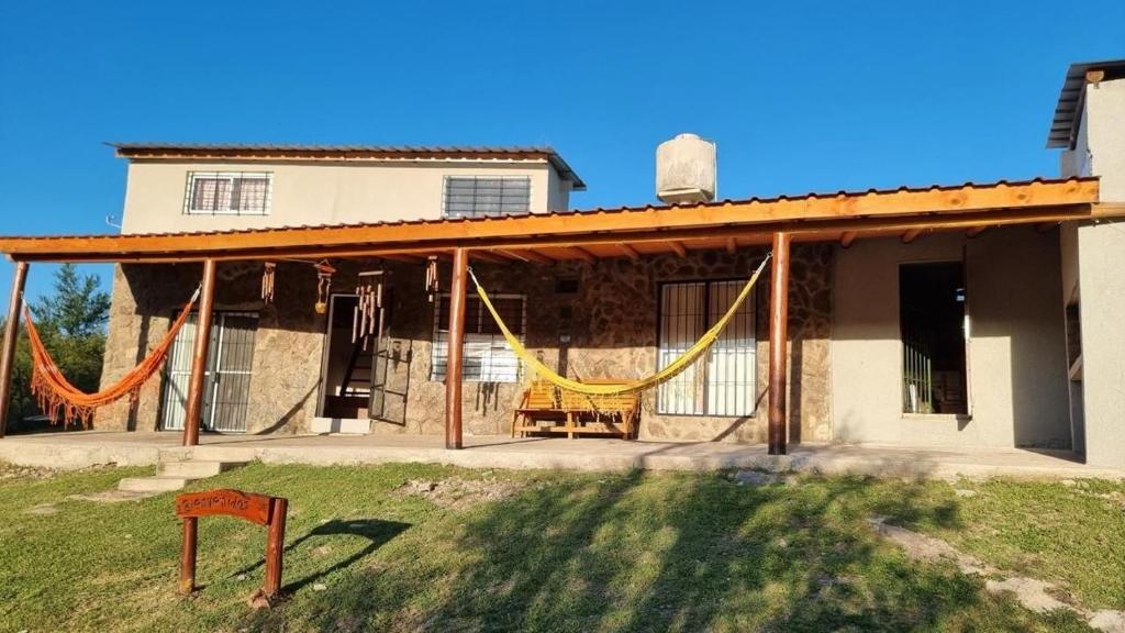 a house with a porch with yellow hammocks on it at casa rustica dos dormitorios con pileta in Huerta Grande