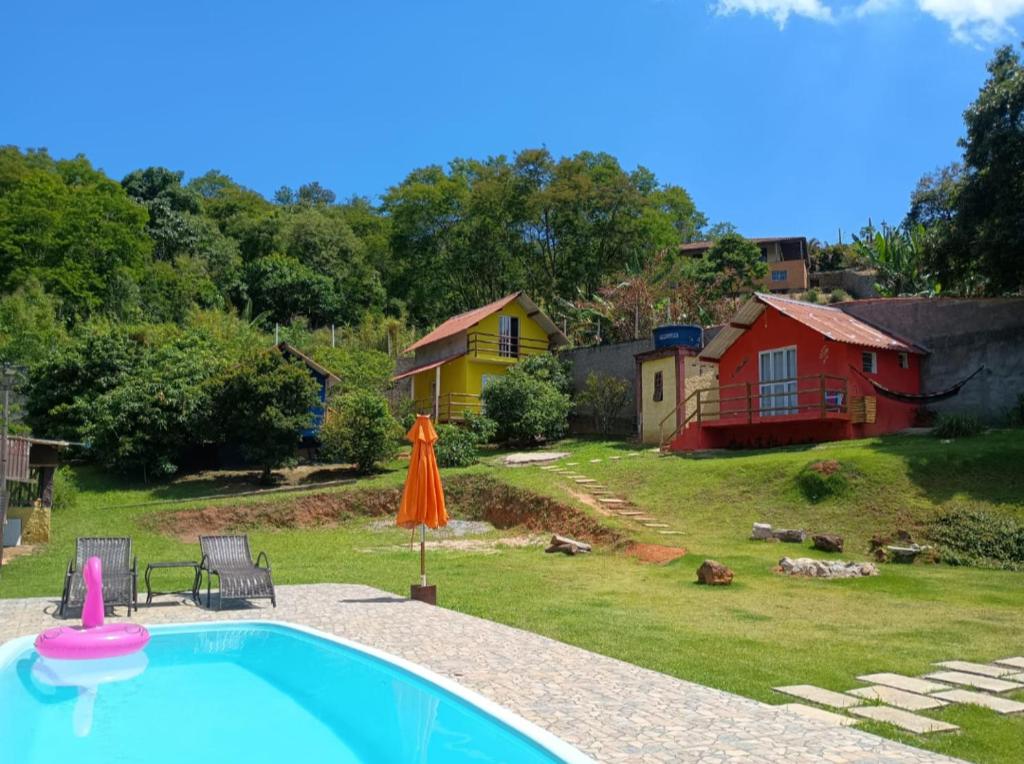 a swimming pool with an umbrella and a house at Chalé Pedacinho do Céu in Mairiporã