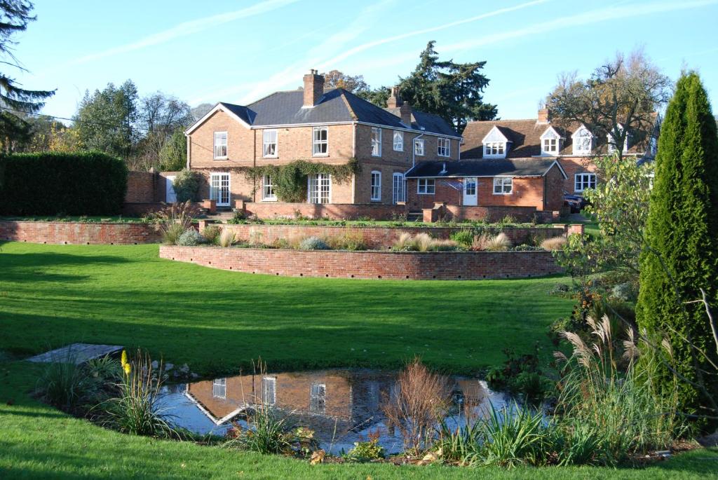 une grande maison avec un étang en face de celle-ci dans l'établissement Rookwood Farmhouse B&B, à Newbury