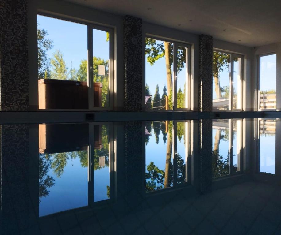 Indoor pool with floor-to-ceiling windows reflecting trees and sky, serene still water and daylight.