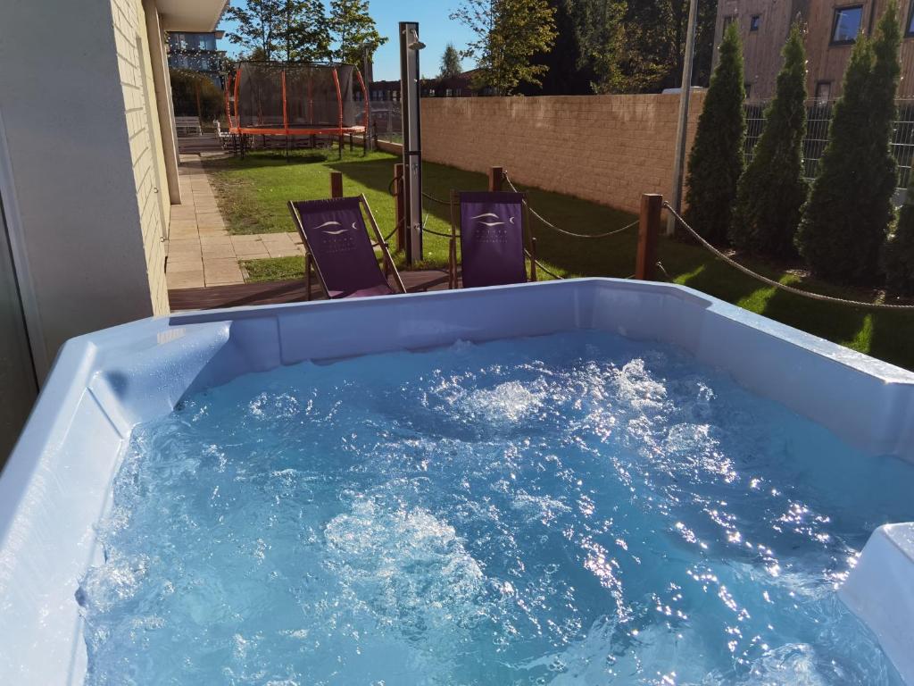 Outdoor bubbling hot tub with deck chairs, sunny garden backdrop and trampoline, inviting relaxation.