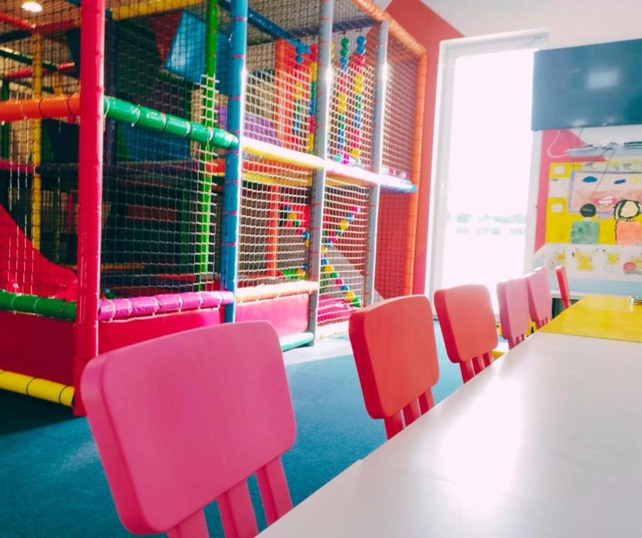 Children's playroom with pink chairs at table and colorful soft-play climbing structure, bright playful atmosphere.