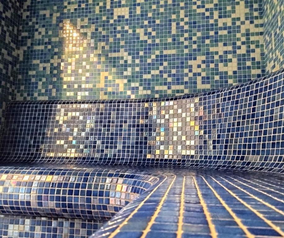 Curved mosaic-tiled steam room bench in blue tones, reflective tiles creating tranquil spa vibe.