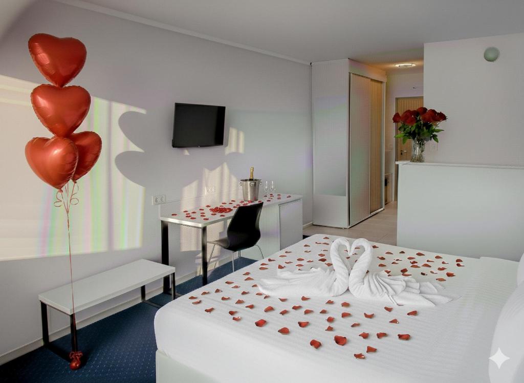 Romantic hotel room with bed swans, scattered rose petals, red heart balloons, desk with champagne.