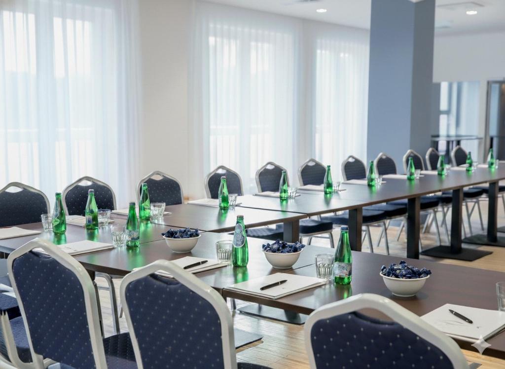 Bright conference room with long tables, bottled water, notepads, and rows of chairs.