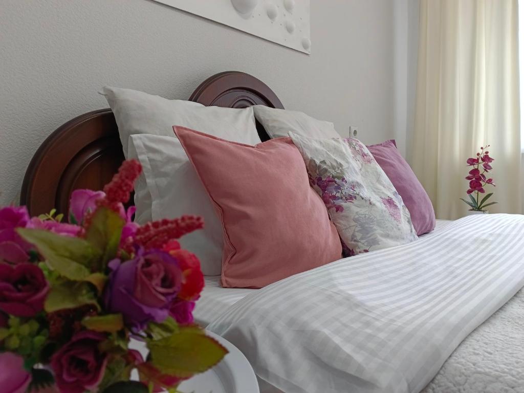 a bed with pink and white pillows and a vase of flowers at Nectar Apartments in Aktobe