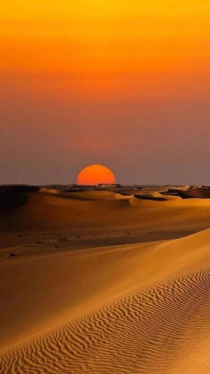 a sunset in the desert with the sun in the horizon at Bivouac Porte du Désert in Mhamid