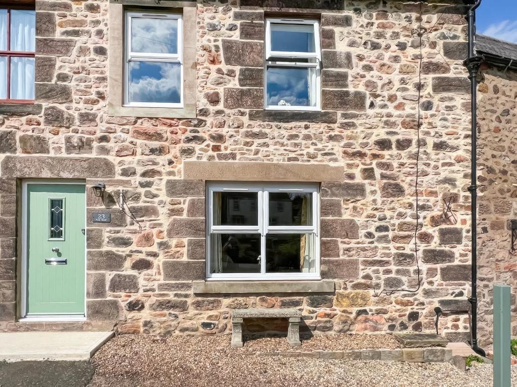 a stone house with a green door and windows at Number 23 in Wooler