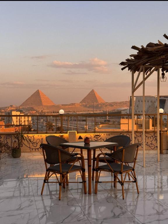 a table and chairs on a roof with pyramids in the background at Sunshine Pyramids& Grand Museum View in Cairo