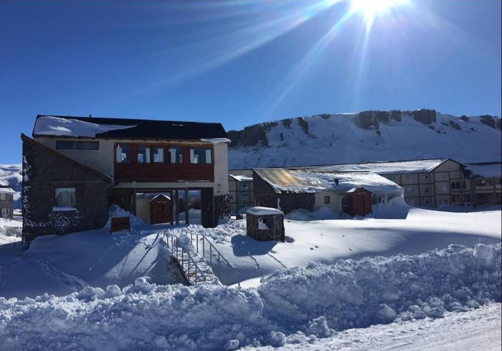 a house covered in snow with the sun behind it at Cabañas Las Cascadas in Caviahue