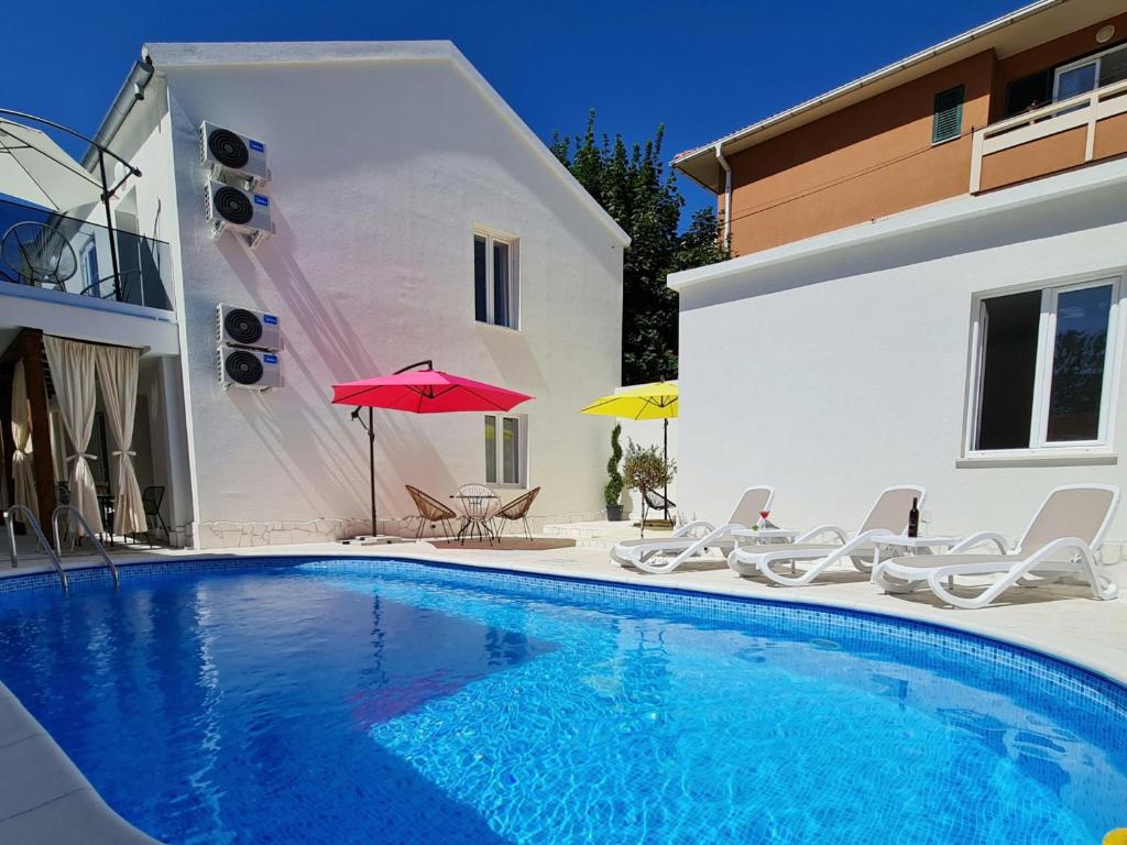 a swimming pool with chairs and umbrellas next to a building at AURA Apartments Novalja in Novalja