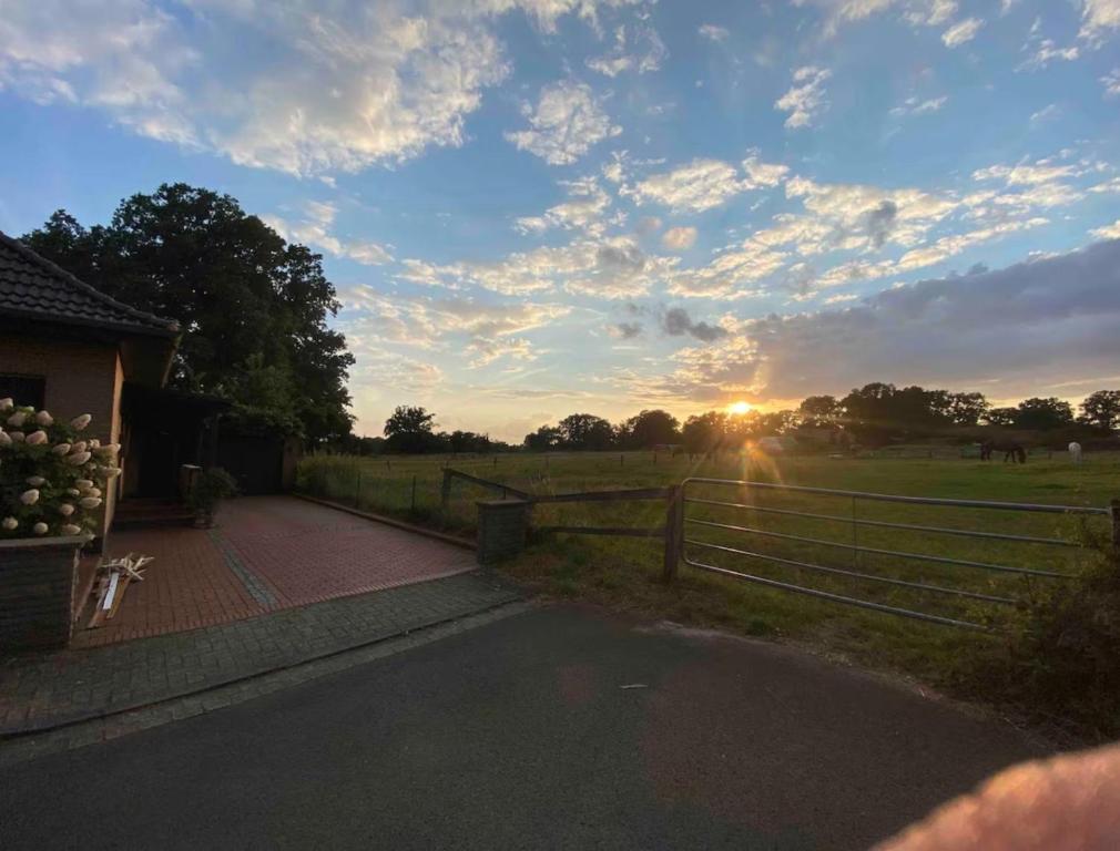 a sunset over a field with a fence and a road at Schöne Wohnung an einer Pferdeweide in Borstel