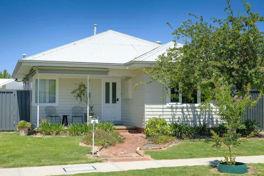 a white house with a tree in the front yard at Cute Cummings St Cottage in Wodonga