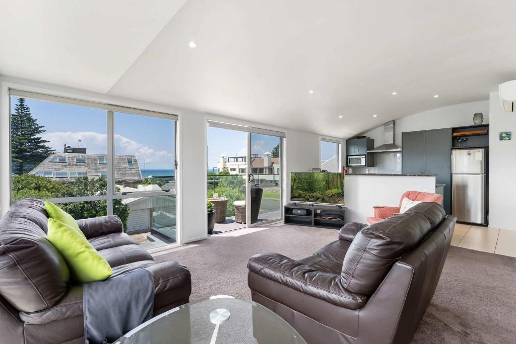 a living room with two leather couches and a kitchen at Longbeach Ocean Paradise in Mount Maunganui