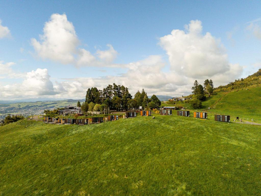 a green hill with houses on a green field at Aorangi Peak Cabins 2 by Tiny Away in Rotorua
