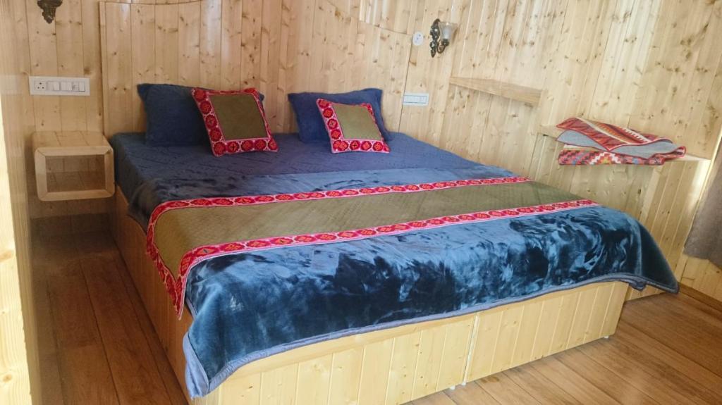 a bed in a wooden room with blue sheets and pillows at Shiva cottage in Kullu Manali