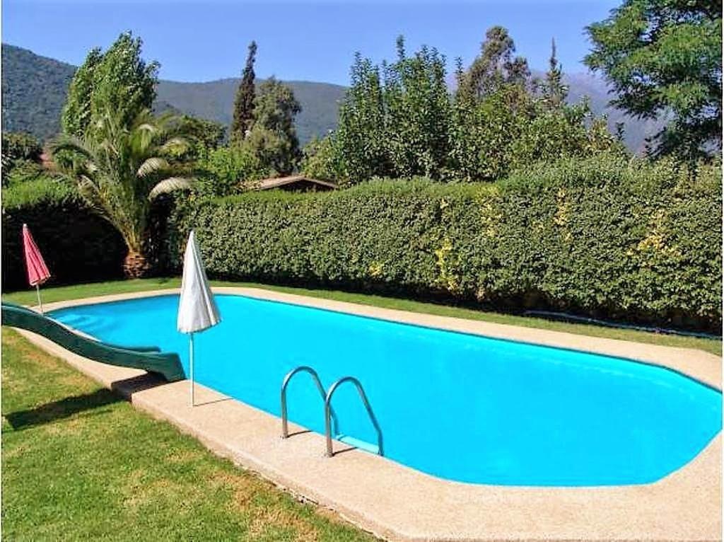 a blue swimming pool with an umbrella next to a hedge at Casa Plaza Los Caballos in Olmué