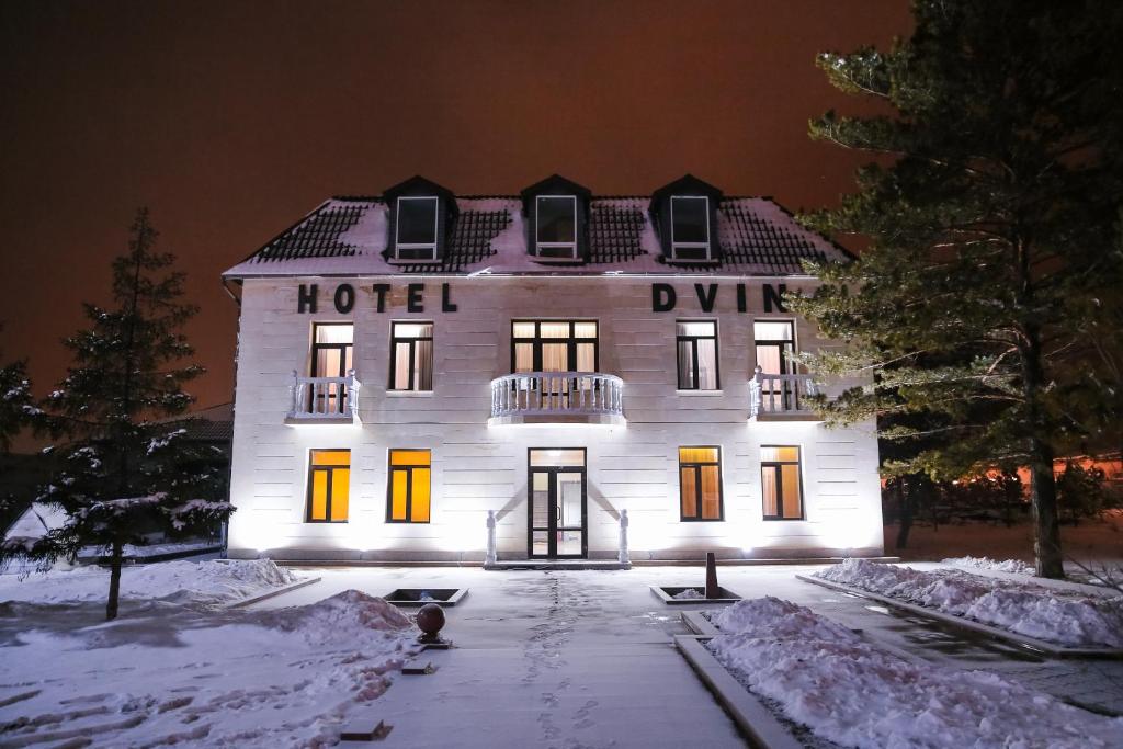 um grande hotel branco com luzes na neve em Dvin Hotel em Pavlodar