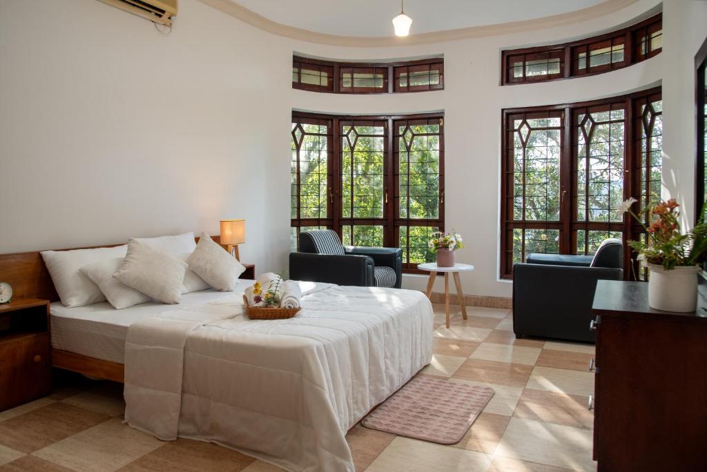 a bedroom with a bed and chairs and windows at Whispering Trees in Kandy
