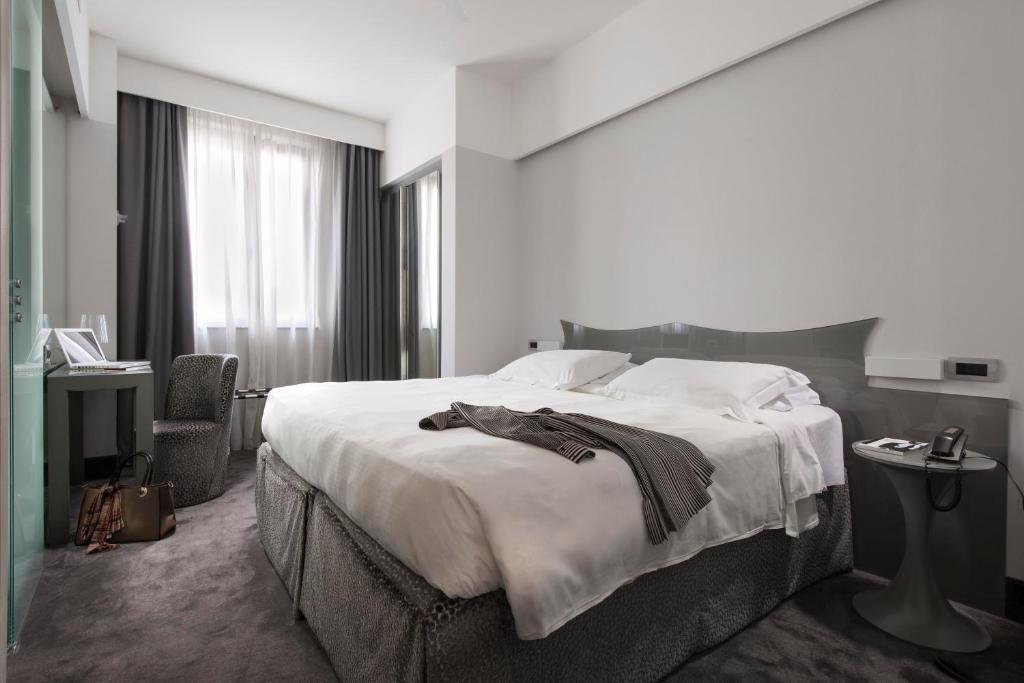 a white bedroom with a large bed and a chair at Hotel Berna in Milan