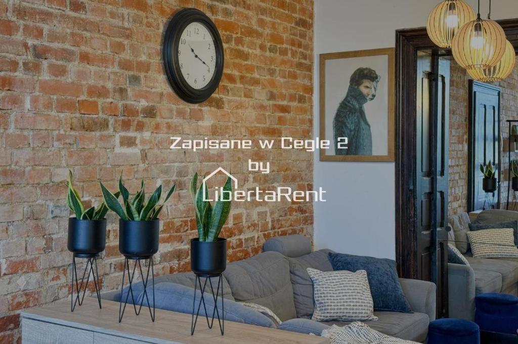 a living room with a couch and a clock on a brick wall at Zapisane w Cegle by LibertaRent in Świdnica