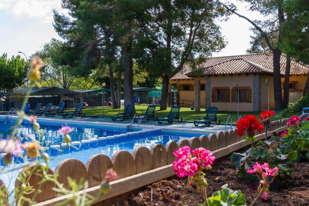 a swimming pool with a house and flowers at Camping-Bungalows Altomira in Navajas