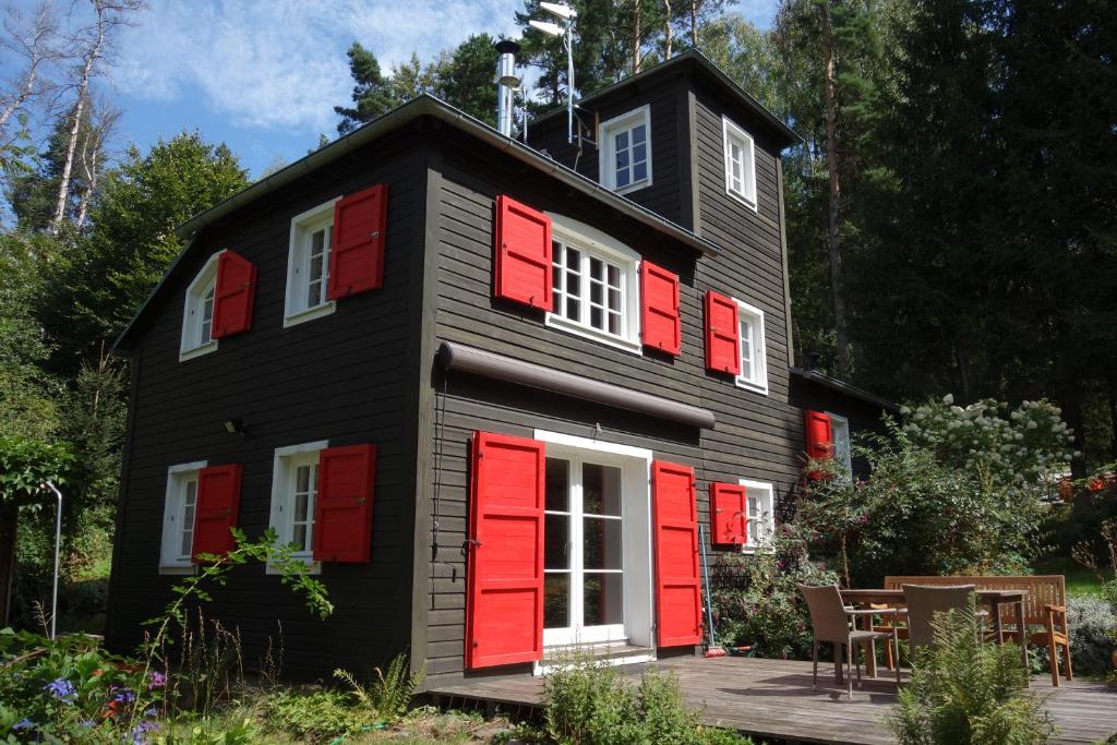 a black house with red shutters and a deck at Ferienhaus Malepartus Sächsische Schweiz in Bad Gottleuba