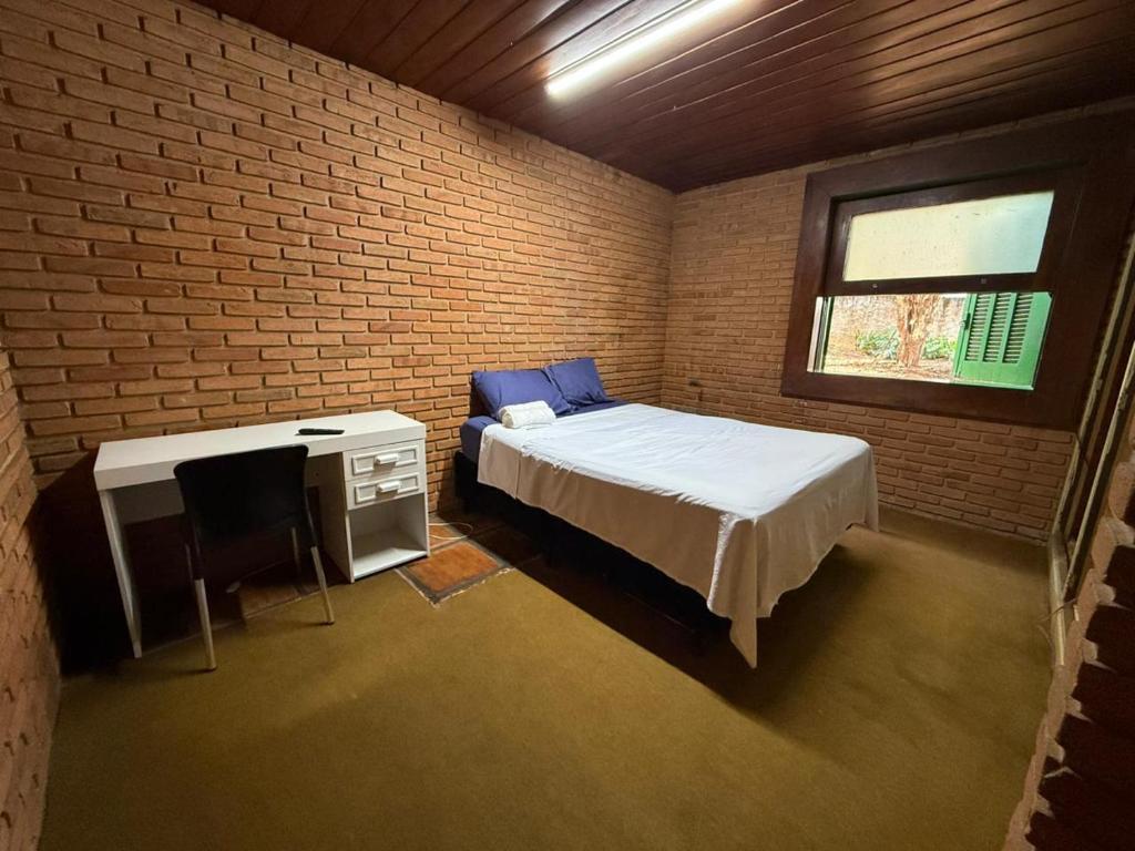 a bedroom with a bed and a desk and a brick wall at Quarto confortável no Centro in Botucatu