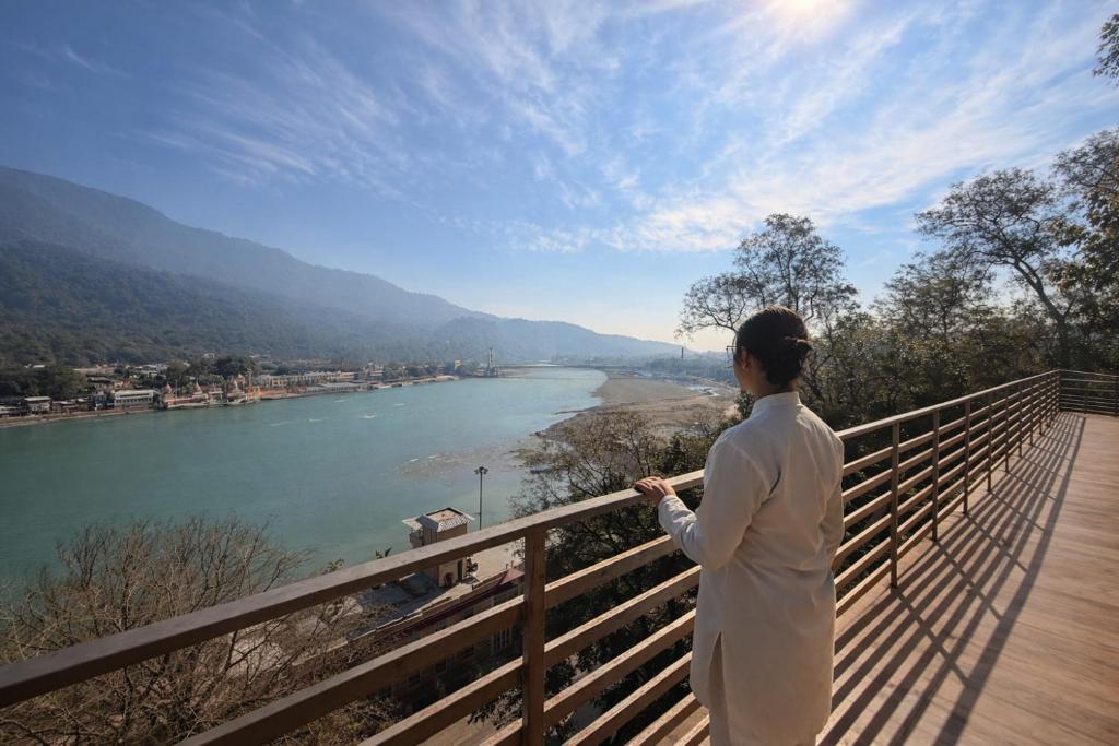 a woman standing on a balcony looking at a river at Yog Niketan Villa in Rishīkesh