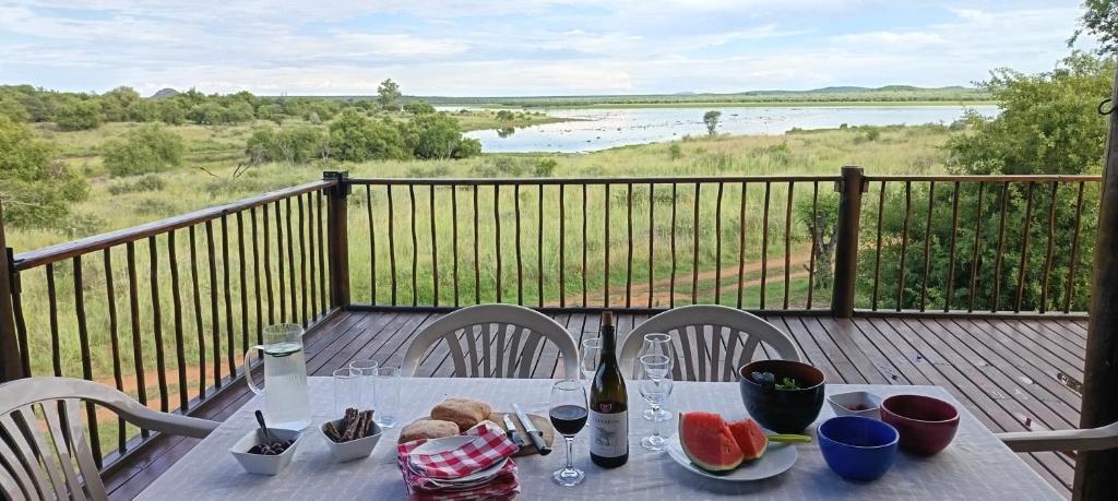 a table with a bottle of wine and fruit on a balcony at Vaalkop Dam Reserve Log Cabin, Self-Catering, Beestekraal in Beestekraal