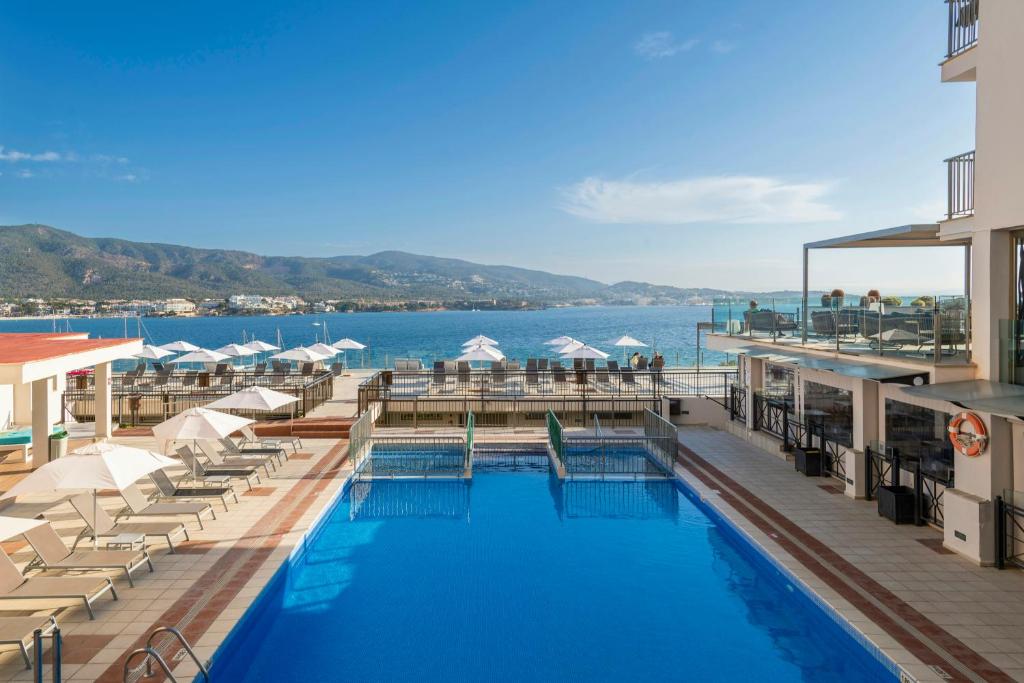 a swimming pool with chairs and umbrellas and the water at Leonardo Royal Hotel Mallorca Palmanova Bay in Palmanova