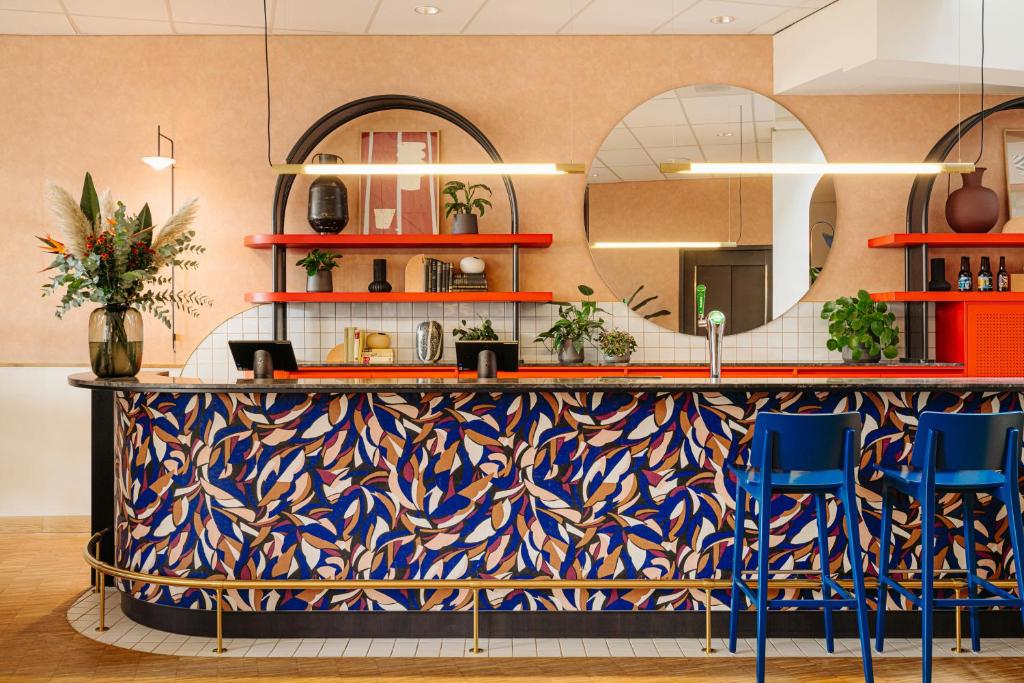a lobby with a counter with blue chairs and a mirror at Leonardo Hotel Groningen City Center in Groningen