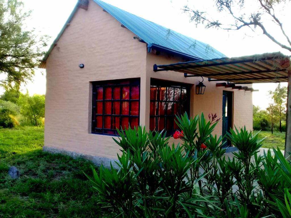 a small white house with red curtains in the window at Cabaña La Escondida in Villa de la Quebrada