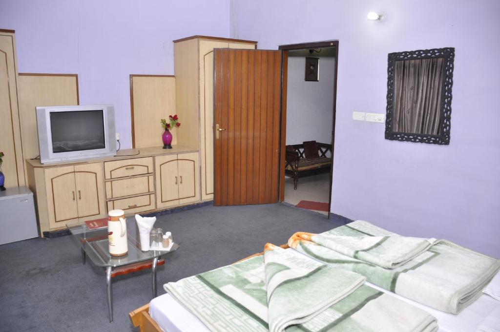 a room with a bed and a tv and a table at Hotel Pratiksha in Morādābād