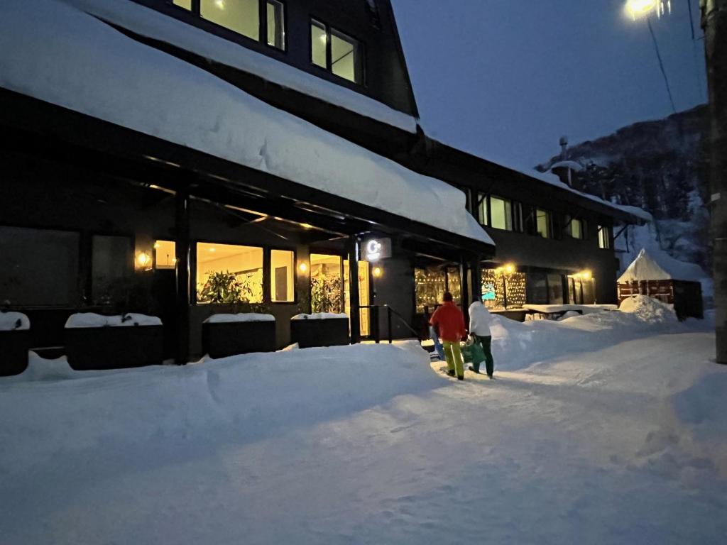 two people walking in the snow in front of a building at Ski-in, Ski-out Iwatake Apartments in Hakuba