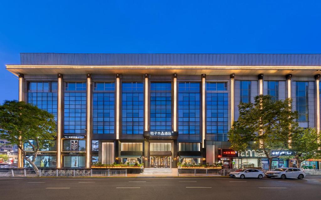 a large glass building with cars parked in front of it at Orange Crystal Hotel Yantai Binhai Square in Yantai