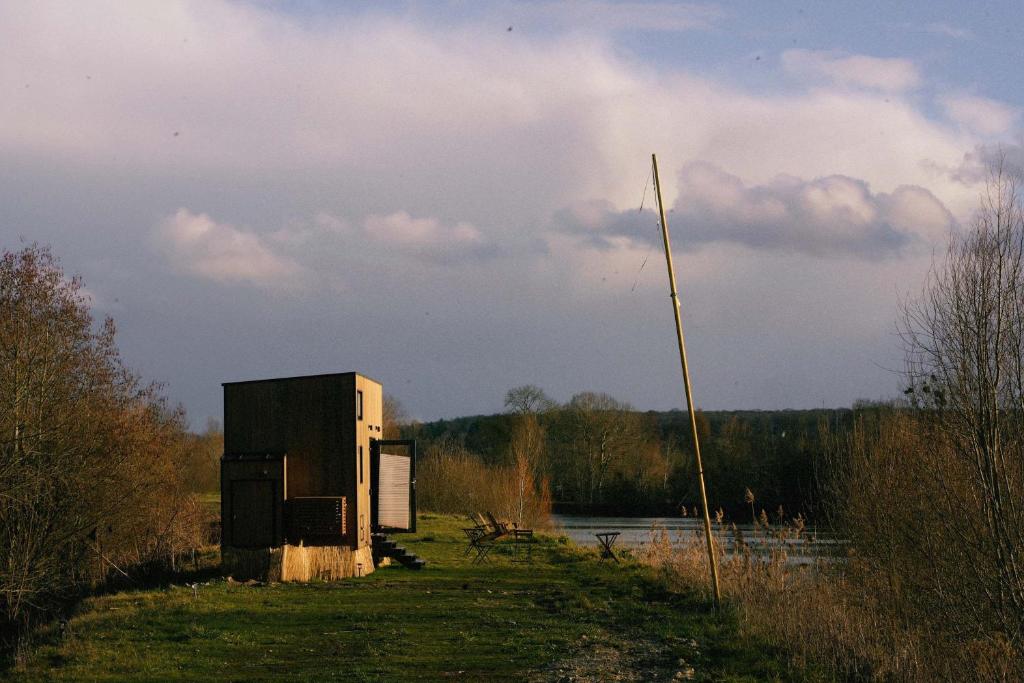 a small shack in a field next to a body of water at Ezy House 2 by Tiny Away in Ézy-sur-Eure