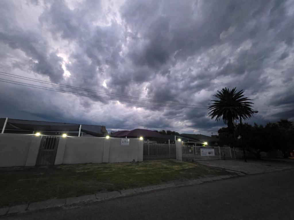 a cloudy sky with a house and a fence at Soliha Guesthouse in Trichardt