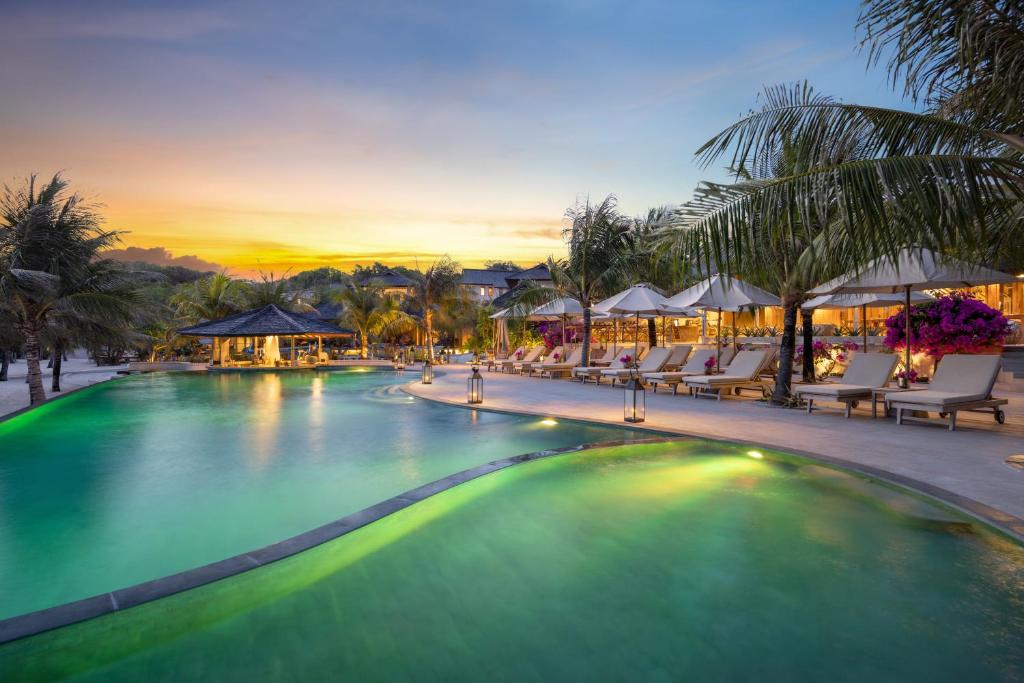 a large swimming pool with chairs and a sunset at Eliana Resort And Spa in Nembrala