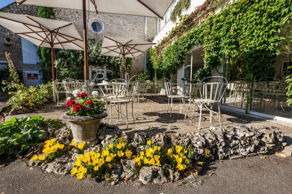 eine Terrasse mit Tischen, Stühlen, Blumen und Sonnenschirmen in der Unterkunft Hostellerie De Bretonnière - Groupe Logis Hotels in Beaune