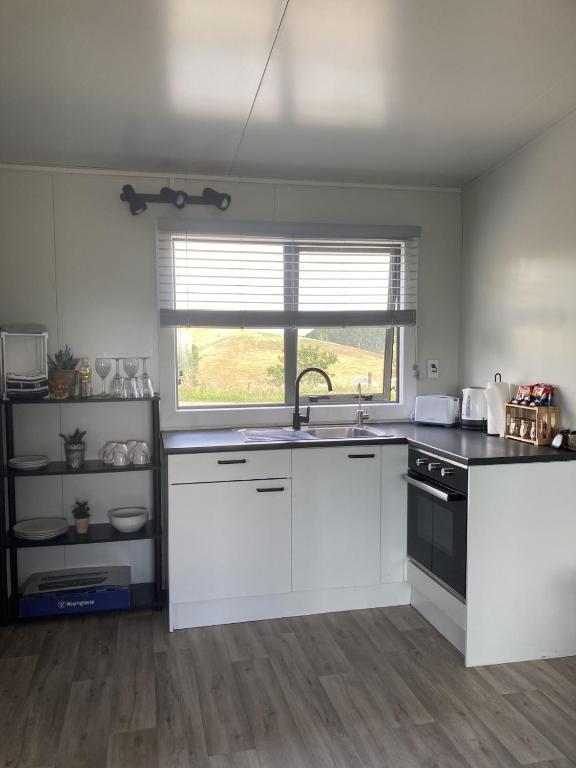 a kitchen with white cabinets and a sink and a window at Hideaway on Honikiwi in Otorohanga