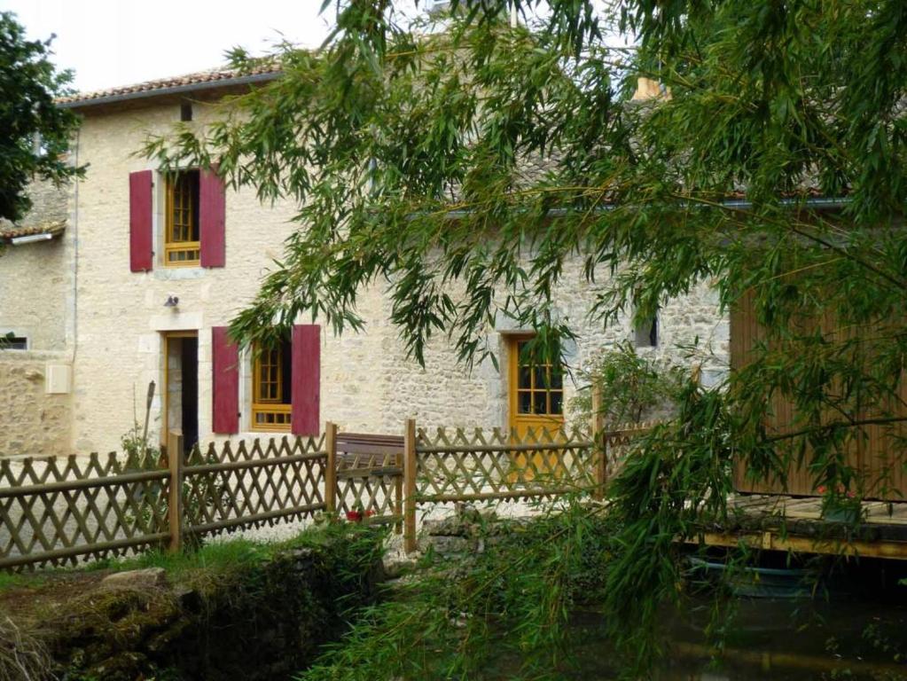 a stone house with red shutters and a wooden fence at Le moulin de preuillé in Valence en Poitoux