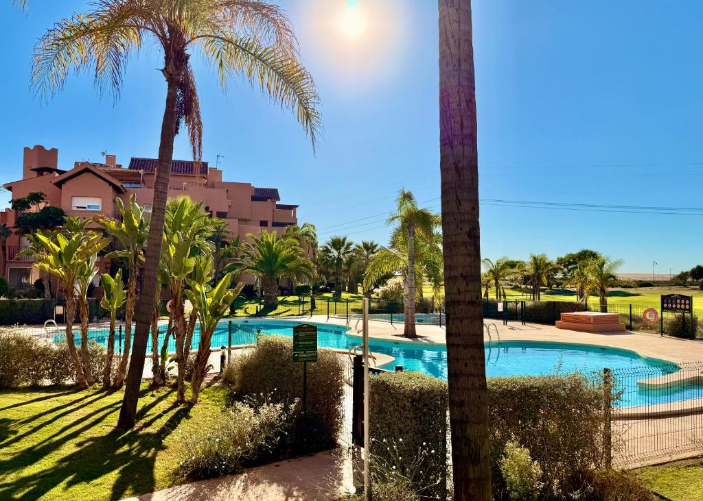 a pool with palm trees and a building in the background at Calma Suite Apartment - Mar Menor Golf Resort in Torre-Pacheco